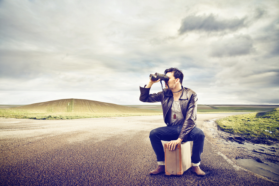 writer sitting on suitcase trying to find paid clients with binoculars