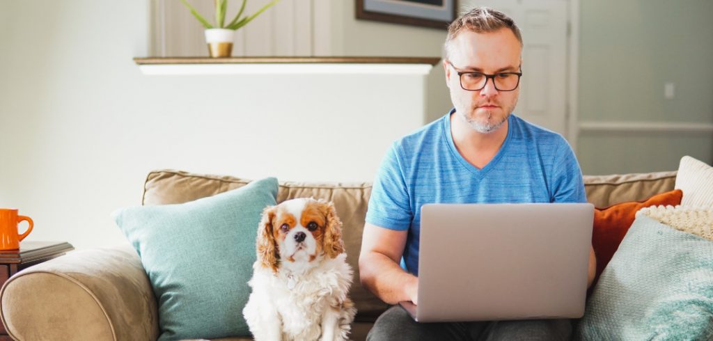 man working on laptop with dog on couch