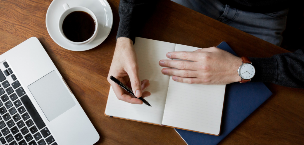 hands writing in notebook on desk