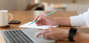 Woman writing article submission on paper and computer