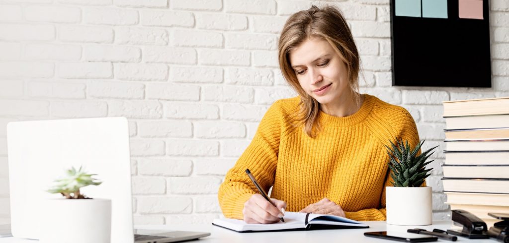 woman getting better at writing on paper pad and laptop