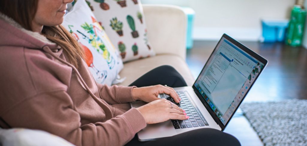 woman on couch writing email subject line on laptop